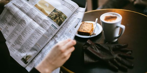 image of someone reading a newspaper with coffee and bread